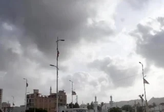 Cloudy sky over Karachi streets with high palm trees swaying in strong sea winds.